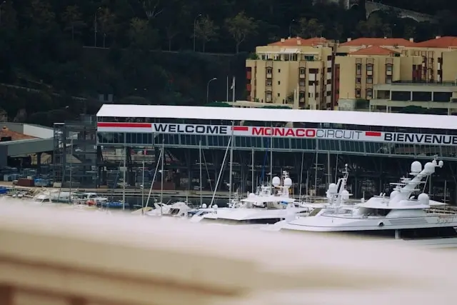 Welcome to Monaco Circuit sign above Port Hercules with white superyachts docked in the harbor below