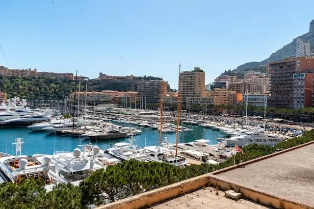 Panoramic view of Monte Carlo harbor filled with luxury yachts and sailboats against Monaco's coastal cityscape and mountains