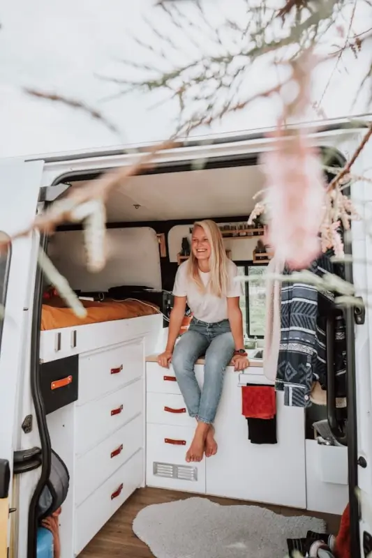 A smiling woman sitting inside a well-organized campervan with a cozy interior, ready for a road trip getaway in spring