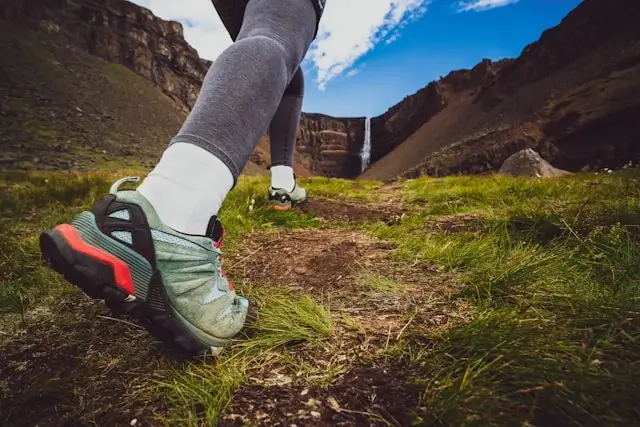Woman wearing trail sneakers on a rugged outdoor path with a waterfall in the background