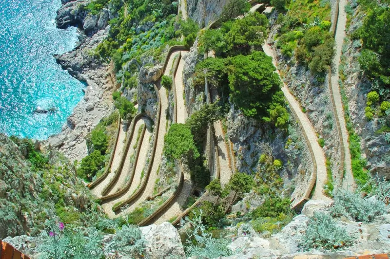Winding switchback path of Via Krupp carved into the cliff face descending to the turquoise waters below