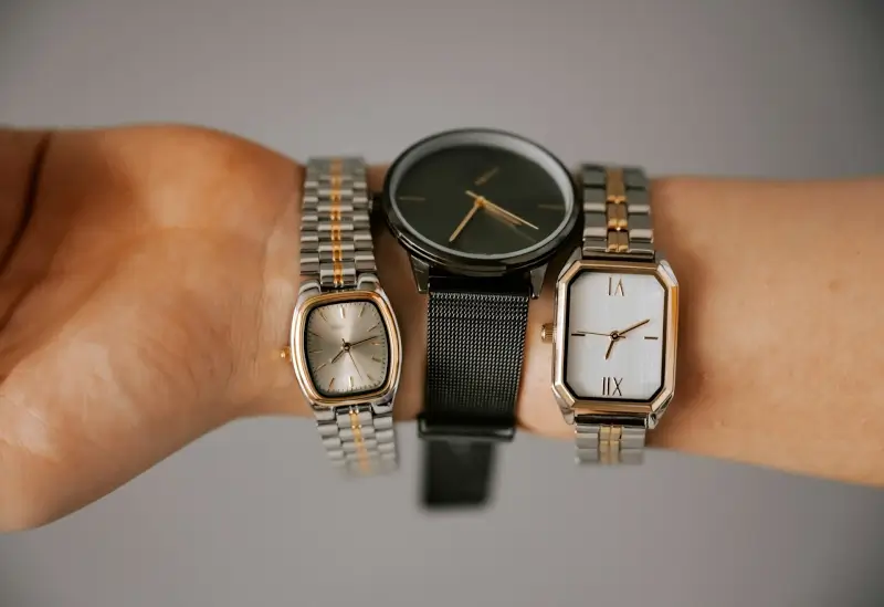 A watch collector wearing three different timepieces on one wrist, showcasing a variety of styles including square, round, and rectangular designs