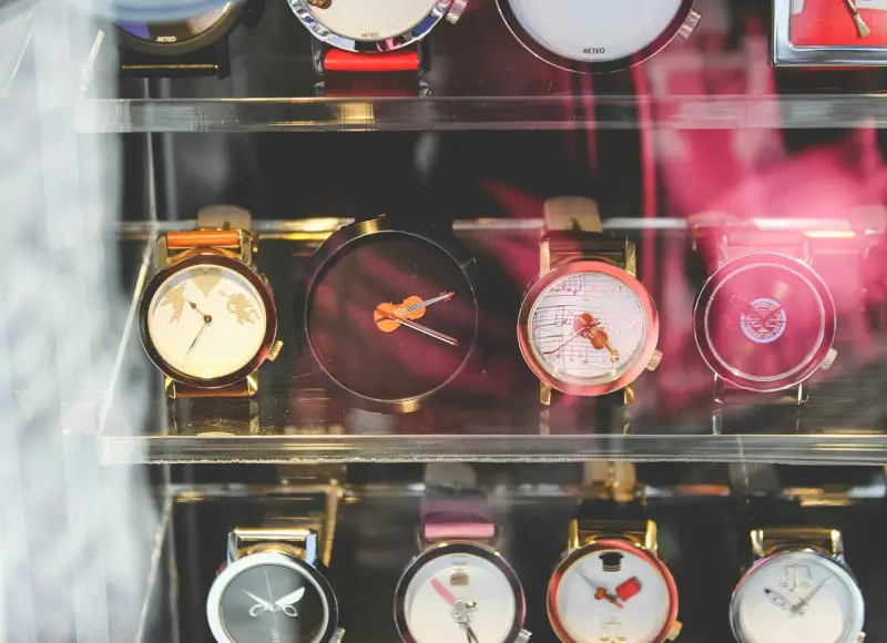 A watch shop display case showcasing a collection of unique artistic timepieces with decorative dials featuring musical and figurative designs