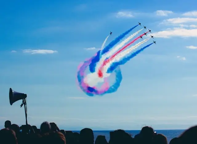 Crowd watching aerobatic team perform loop maneuver with colorful smoke trails against blue sky