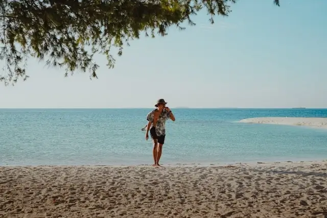 A man walking alone on a quiet sandy beach with calm turquoise water, representing travel after major life changes