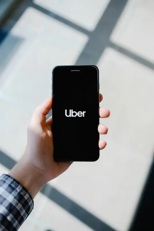 A person holding a smartphone displaying the Uber app logo, representing how rideshare companies operate as passenger transportation services