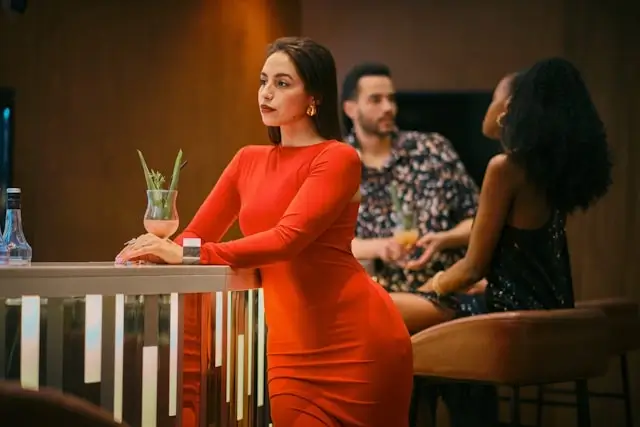 A solo traveler enjoying a night out at a stylish bar, dressed in red with a cocktail in front of her