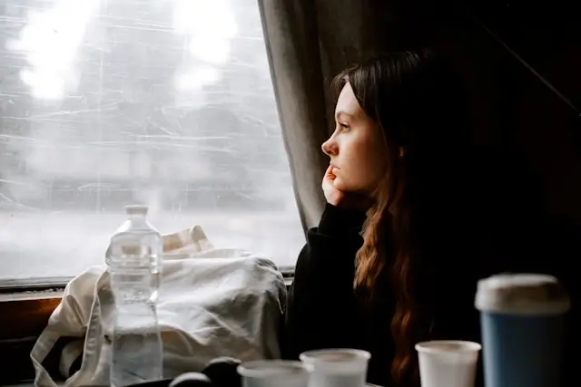 A woman traveling alone on a train, gazing thoughtfully out the window while reflecting on major life changes