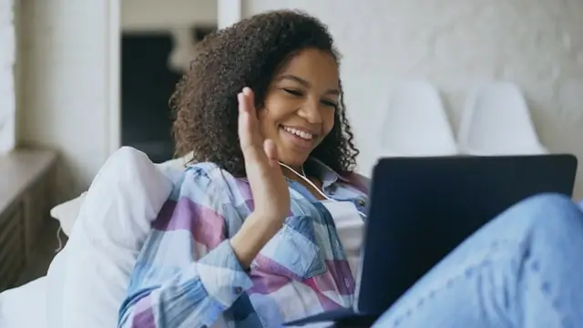 A young woman waving and smiling during a video chat session on her laptop at home