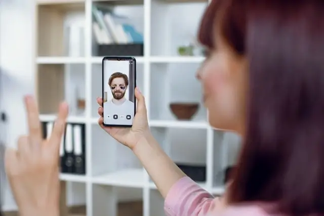 A woman holding a smartphone and video chatting with a man on screen