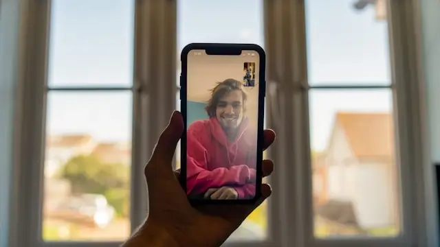 A person holding a smartphone to chat with a smiling stranger on a video call by a sunlit window