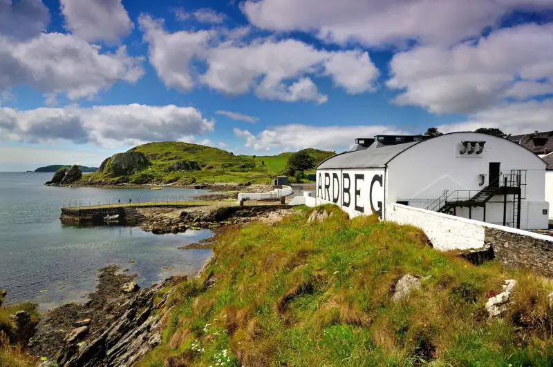 White warehouse buildings of Ardbeg distillery overlooking a calm Scottish sea loch