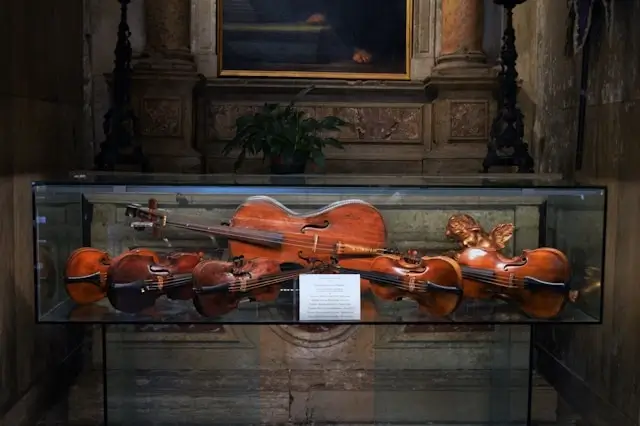 A collection of antique Baroque violins displayed in a glass case inside a historic building