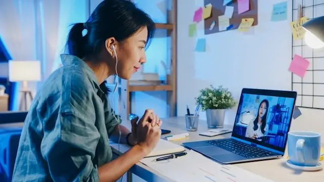 A young woman wearing earphones and building an online friendship through a video chat on her laptop late at night