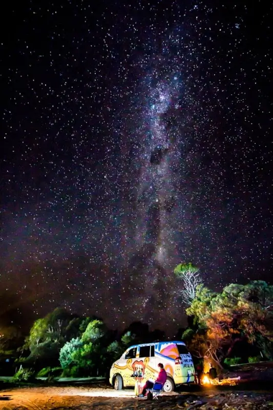 off-grid van camping under the Milky Way at Freycinet Tasmania with a glowing campfire and native bush surrounds