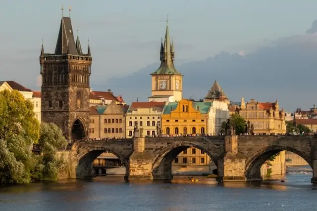 Charles Bridge in Prague with its historic stone arches, Gothic tower, and colorful Old Town buildings along the Vltava River at golden hour