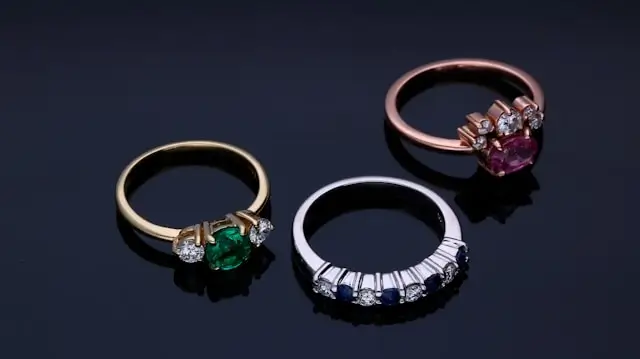 Three gemstone rings for choosing an engagement ring, featuring emerald in yellow gold, sapphire in white gold, and ruby in rose gold