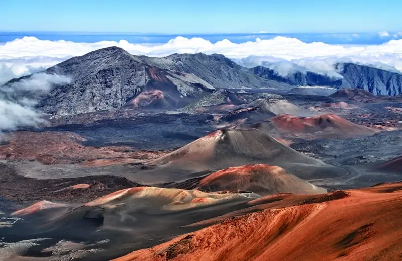 rust-colored cinder cones rising above the clouds inside Haleakala volcano crater in Maui