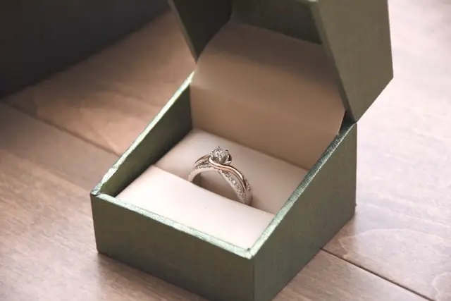 A diamond engagement ring with a twisted band displayed in an open green ring box