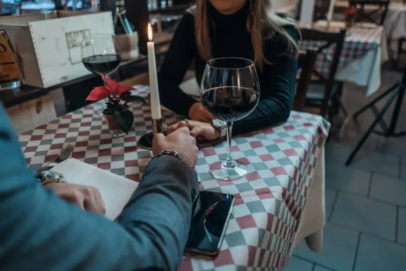 A couple holding hands across a candlelit restaurant table with red wine, capturing the first impression effect in international dating.