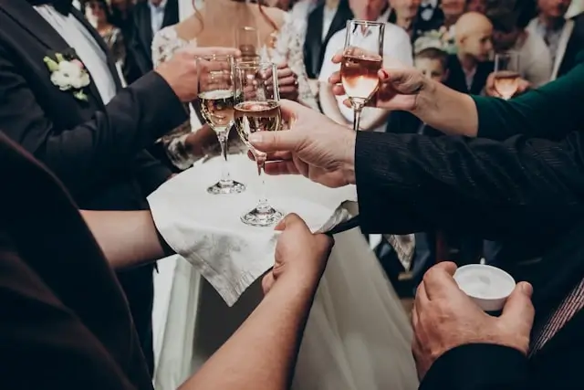 Guests clinking champagne glasses at a formal event with a bride visible in the background