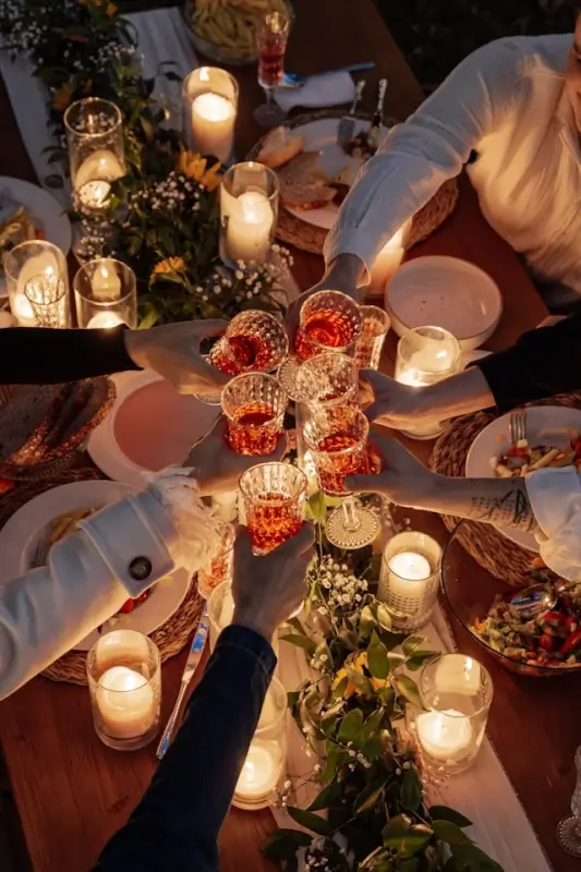 Group of people enjoying social companionship at a candlelit gala dinner, toasting with crystal glasses over a beautifully decorated table with flowers and candles