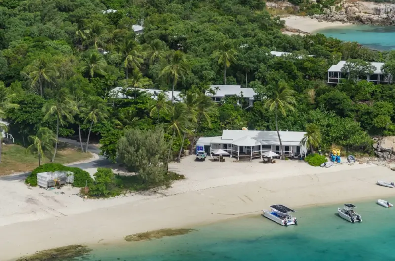 aerial view of a beachfront resort with boats and palm trees on a tropical island near the reef in Queensland
