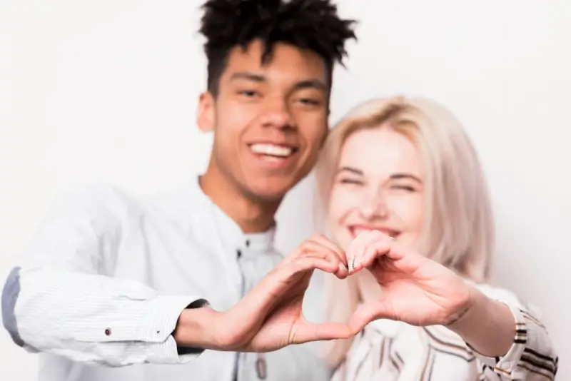 A smiling interracial couple making a heart shape with their hands, reflecting a genuine connection with a Ukrainian woman in an international relationship.