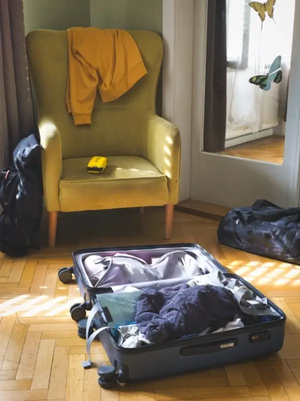 open luggage filled with clothing on a wood floor with bags packed and ready for moving day