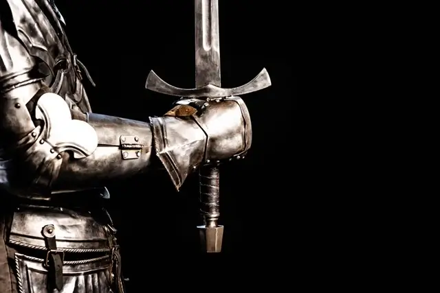 Close-up of a medieval knight's armored arm holding a longsword in combat stance
