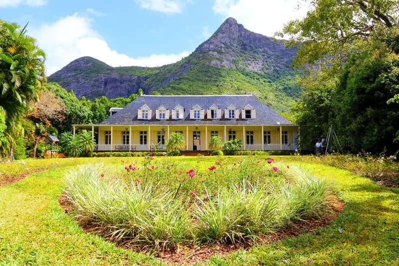 19th-century colonial house at Maison Eureka Mauritius with flowering garden beds and misty mountains in the background