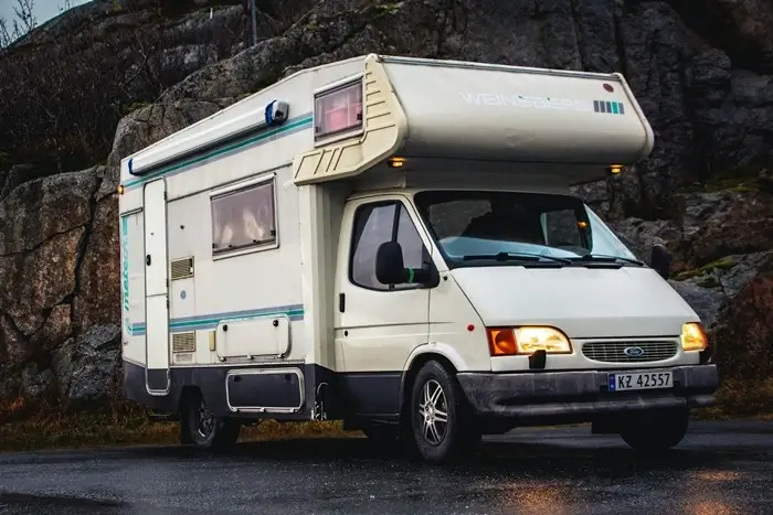 vintage budget campervan with overhead cab parked on a wet road beside large boulders in low light
