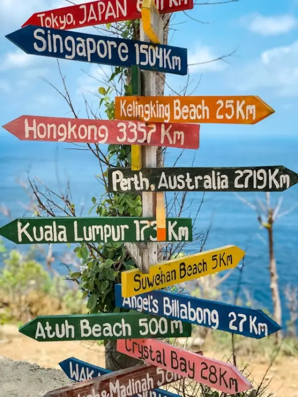 Colorful wooden signpost showing distances to multiple travel destinations including Singapore, Tokyo, Hong Kong, and Perth Australia.