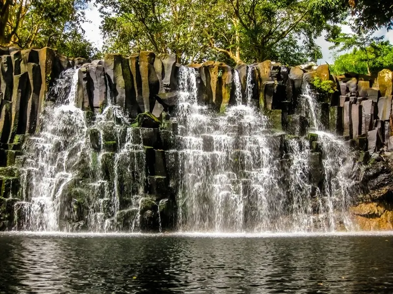 Rochester Falls in Mauritius cascading over dramatic jagged basalt columns into a dark natural pool surrounded by tropical trees