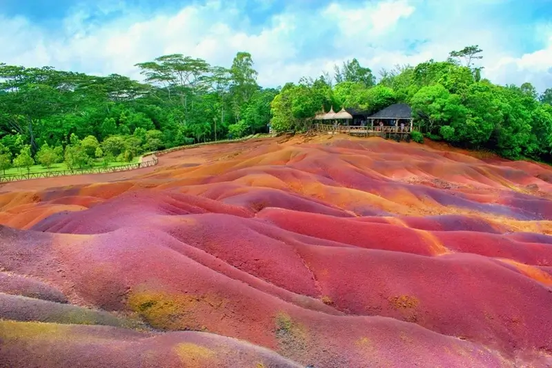Seven Colored Earth of Chamarel in Mauritius with rolling bands of red, orange and purple volcanic soil against a lush green forest backdrop