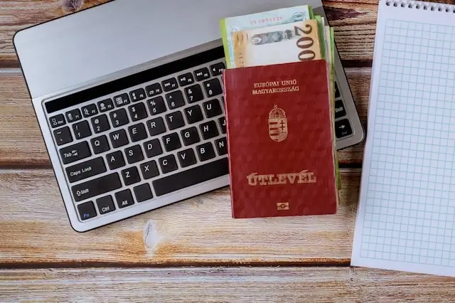 Simple steps for travel planning laid out on a wooden desk with a laptop, passport, cash, and a blank notepad.