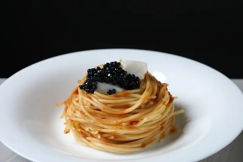 Spaghetti pasta nest topped with black caviar and shaved parmesan on a white plate