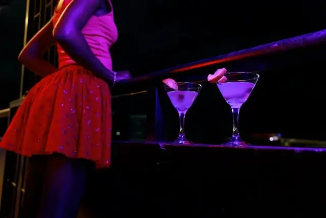 Two martini glasses left unattended on a railing at a nightclub while a woman stands nearby