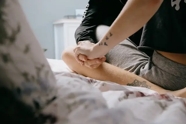 supportive partner holding hands with a trans loved one on a bed
