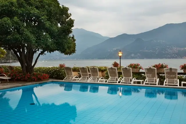 Outdoor pool with lounge chairs and Lake Como mountain backdrop at an EDITION hotel