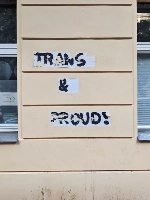trans and proud sign posted on a building wall