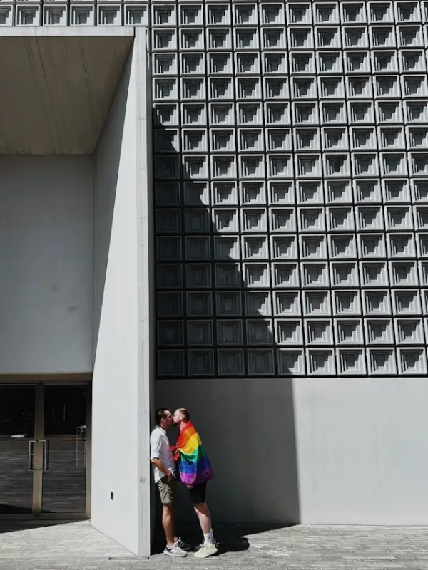 transgender couple kissing outside a modern building with a rainbow pride flag