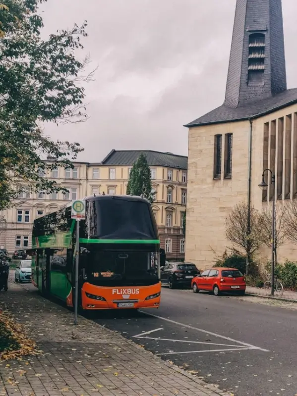 A FlixBus double-decker coach stopped at a city bus stop near a stone church building, illustrating how passenger transport services operate under defined safety standards