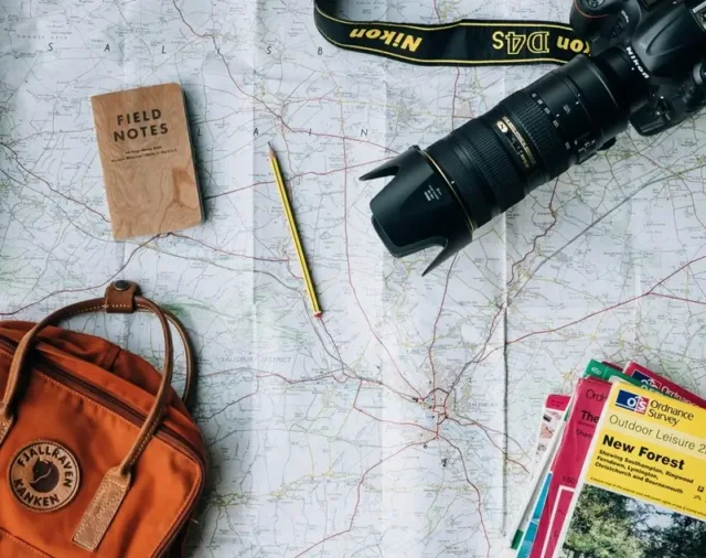 A flat lay of group travel planning essentials including a map, field notes journal, camera, and backpack