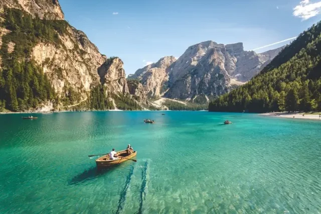 People rowing wooden boats on a stunning turquoise lake with dramatic rocky peaks in the background