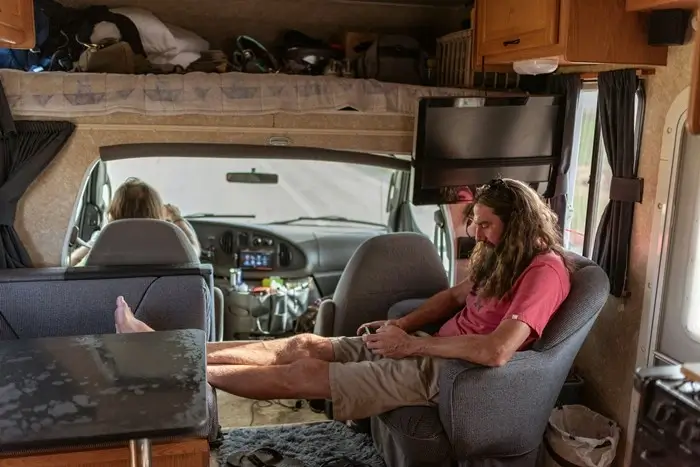 traveler lounging in a campervan living area with feet up, overhead storage, and a second person in the driver's seat