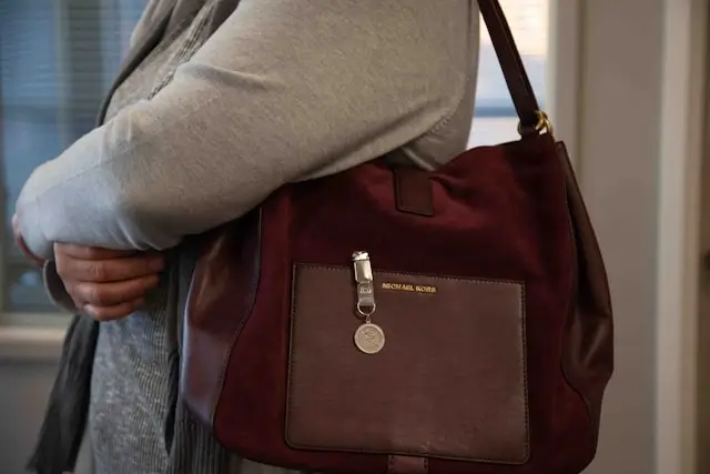 Close-up of a versatile burgundy suede shoulder bag worn by a woman in a grey top