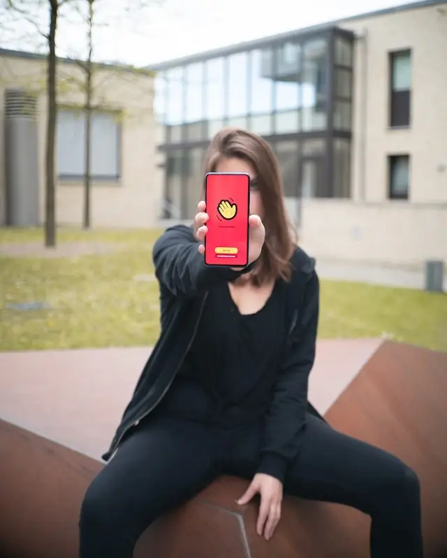 A woman sitting outdoors holding up a smartphone displaying a video chat platform app screen