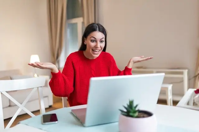 An excited woman in a red sweater gesturing during a video chat with people around the world on her laptop at home
