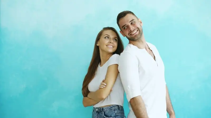 A smiling couple standing back to back against a teal background, showing why first impressions matter in cross-border dating relationships.